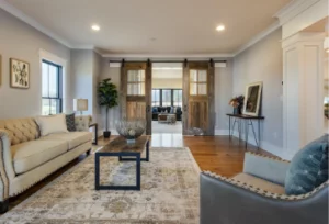 Elegant living room with a beige sofa, hardwood floors, a wooden coffee table, and sliding barn doors leading to the next room.