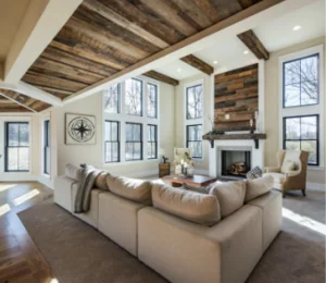 Spacious living room with exposed wooden beams, large windows, a stone fireplace, and a beige sofa facing a coffee table.