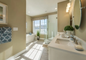 A modern bathroom with a freestanding bathtub, glass-enclosed shower, double vanity with two sinks, a large window, and light brown walls.