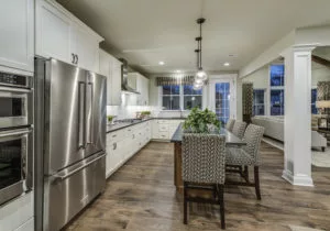 Modern kitchen with stainless steel appliances, a center island with chairs, white cabinets, and hardwood flooring. The space opens up to a living area visible in the background.